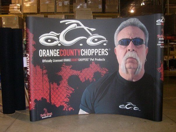 Orange County Choppers display with logo, motorcycle graphic, and Paul Teutul Sr. with sunglasses.