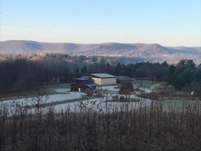 Buildings surrounded by frost-covered fields and trees, with mountains in the background under a blue sky.