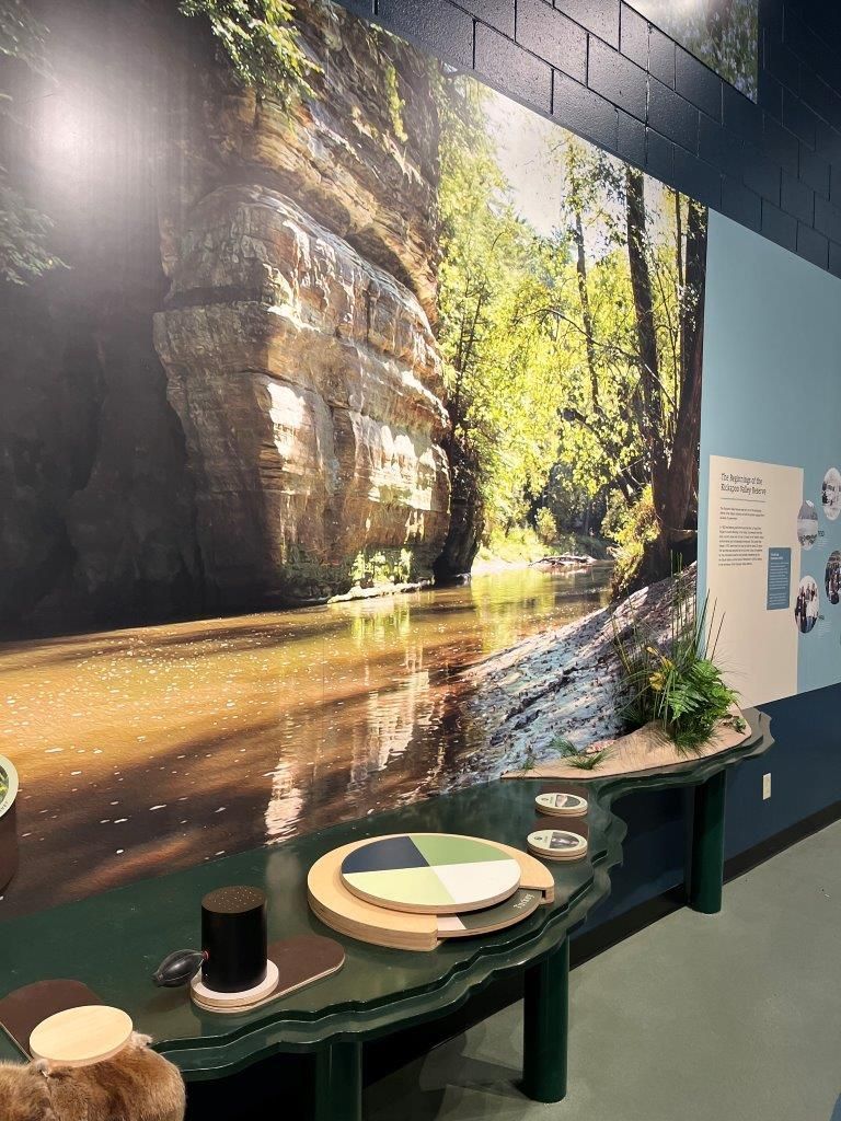 Display showing a river scene mural, with a table featuring interactive elements and text panels.