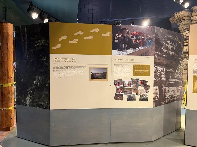 Exhibit panels with text and photos; gold, white, and gray colors. Footprints and people are depicted.