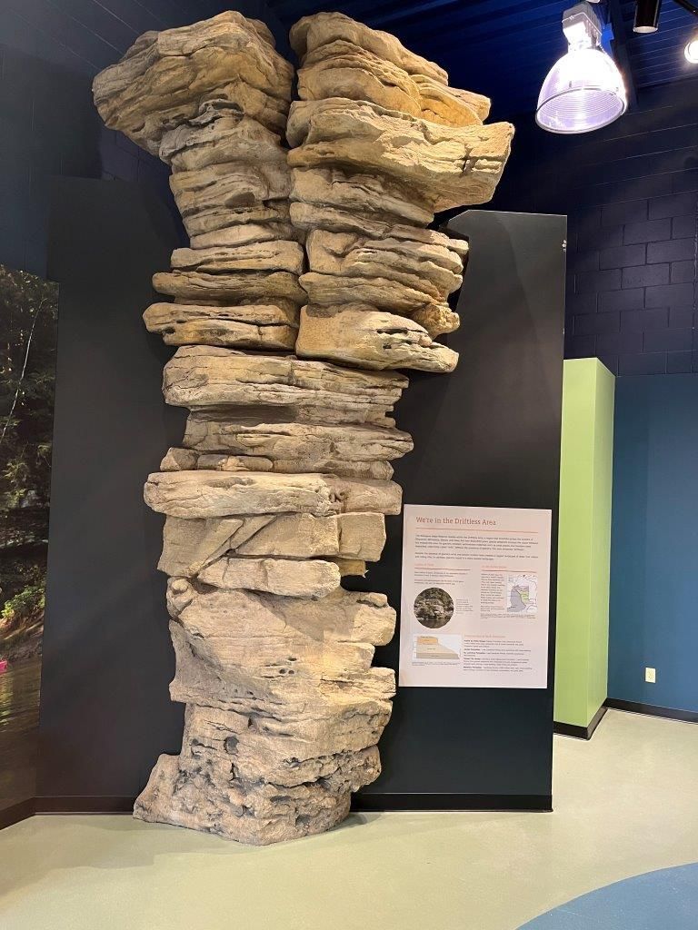Stone rock formation exhibit in a museum. Beige and tan colored rock against a dark gray backdrop.
