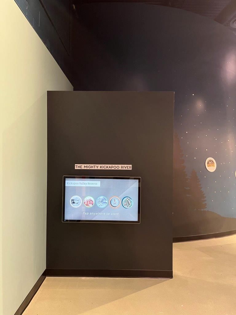 Black display screen on a dark wall with interactive options, next to a pale green wall.