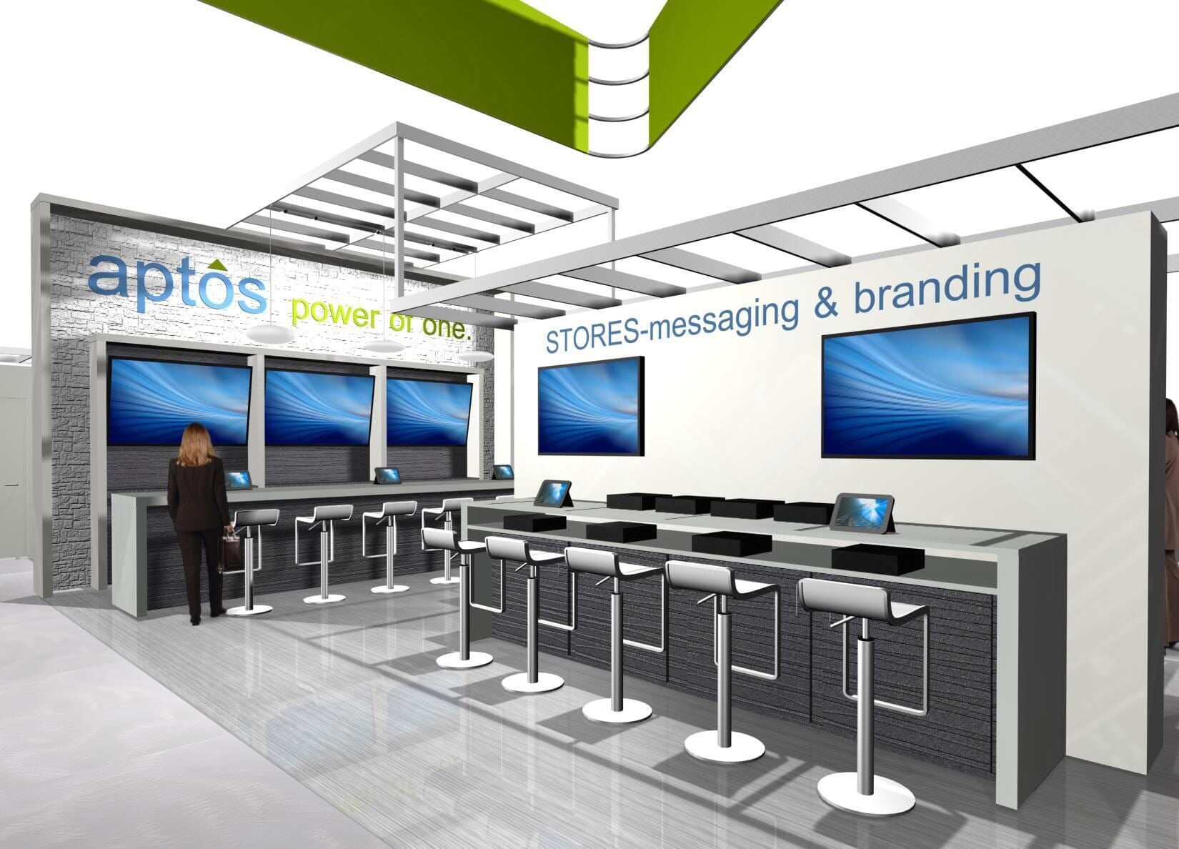 Aptos booth: Multiple computer screens, seating, and branding on display at a trade show.