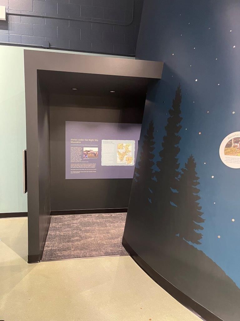Interior view of a museum entrance with dark walls, an exhibit, and a mural of a nighttime forest scene.