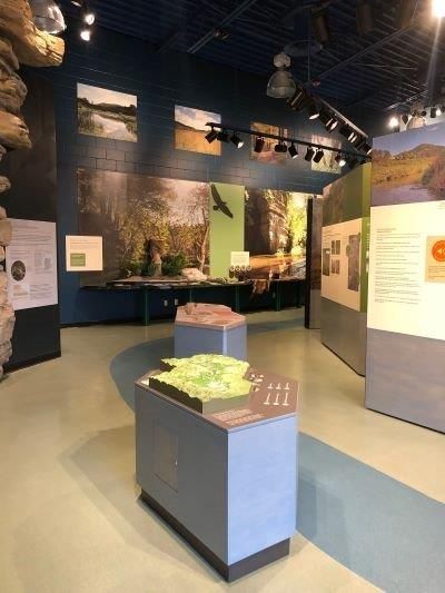 Interior of a museum gallery with displays, landscape photos on walls, and a light blue floor.