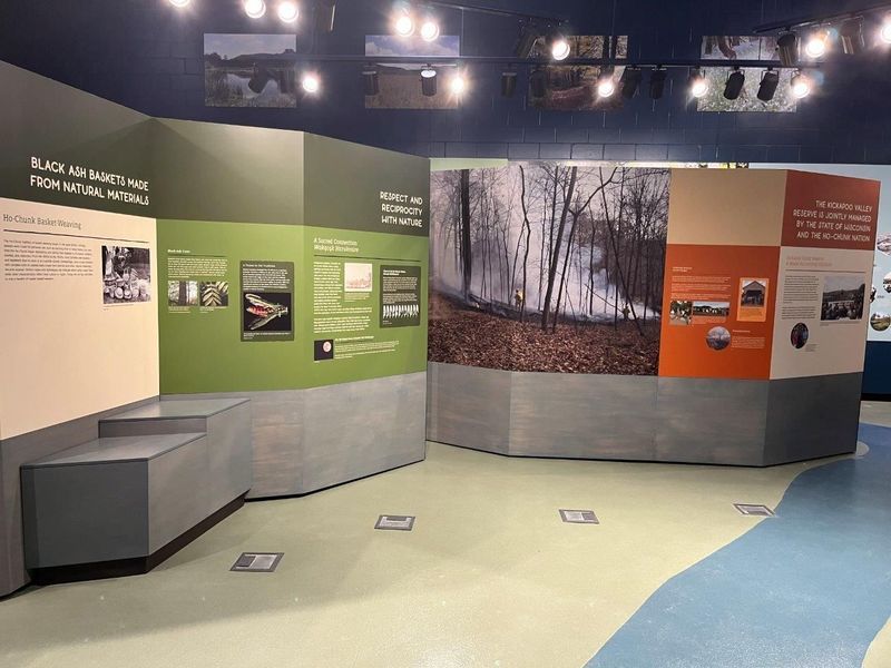Museum exhibit with informational panels and photographs. Walls are various colors: green, orange, and gray. Blue floor.