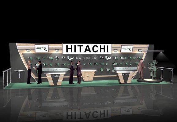 Hitachi booth with products displayed, people interacting. Green flooring, black backdrop. 