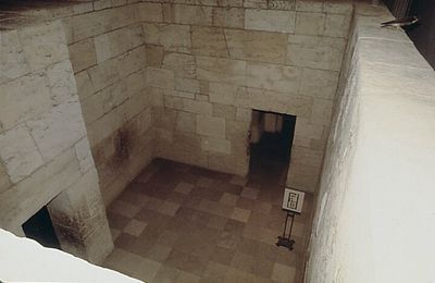 Stone-walled room with a doorway, lit by natural light. The floor is tiled.
