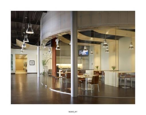 Modern office interior with curved glass walls, dark wood floors, and pendant lights.