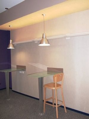 Two modern tables with metal legs, pendant lights, and a wooden stool against a neutral wall.
