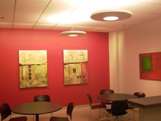 A room with red wall, art, and round tables with chairs. Two disc-shaped lights hang from the ceiling.