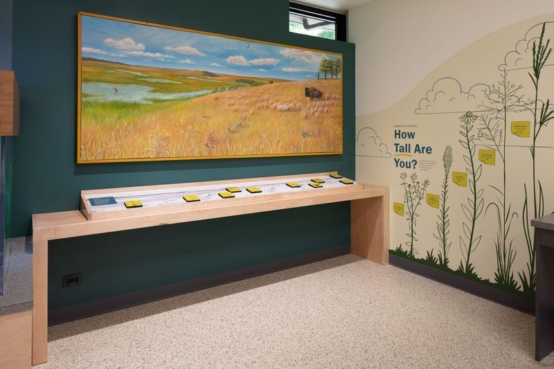 Exhibit with landscape painting, display table, and interactive wall. Green and beige color scheme.