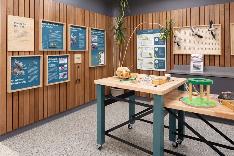 Interior museum exhibit with wood panel walls, informational displays, and activity tables.
