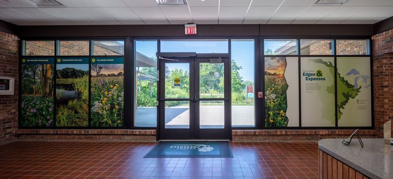 Entrance with glass doors and display windows featuring nature scenes. Red brick wall and tiled floor.