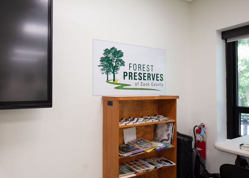 Sign for Forest Preserves of DeKalb County above a wooden bookshelf with brochures; a window is visible.