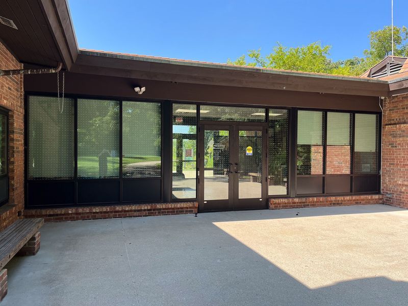 Building entrance with glass doors and windows, brick exterior, and shaded walkway.