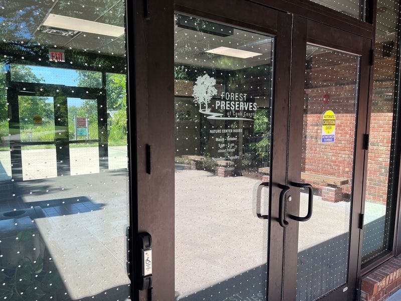 Glass doors to Forest Preserve building. Black handles, white text, dotted design, brick wall visible.