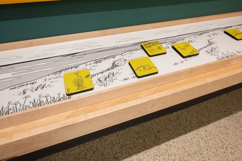 Wooden display with yellow square tiles on a landscape illustration.
