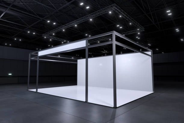 Empty trade show booth with white walls and a black metal frame in a dark hall.