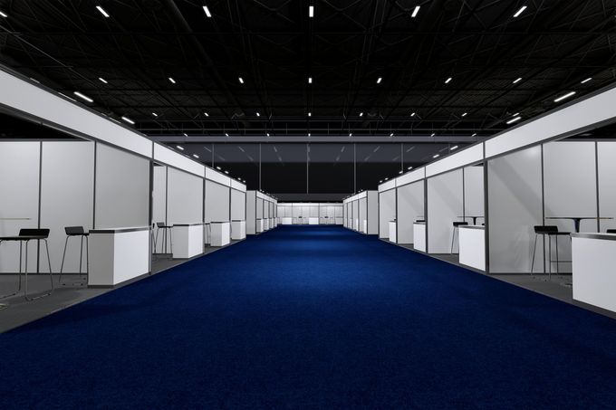 Empty exhibition hall with a blue carpeted aisle and white booth spaces.