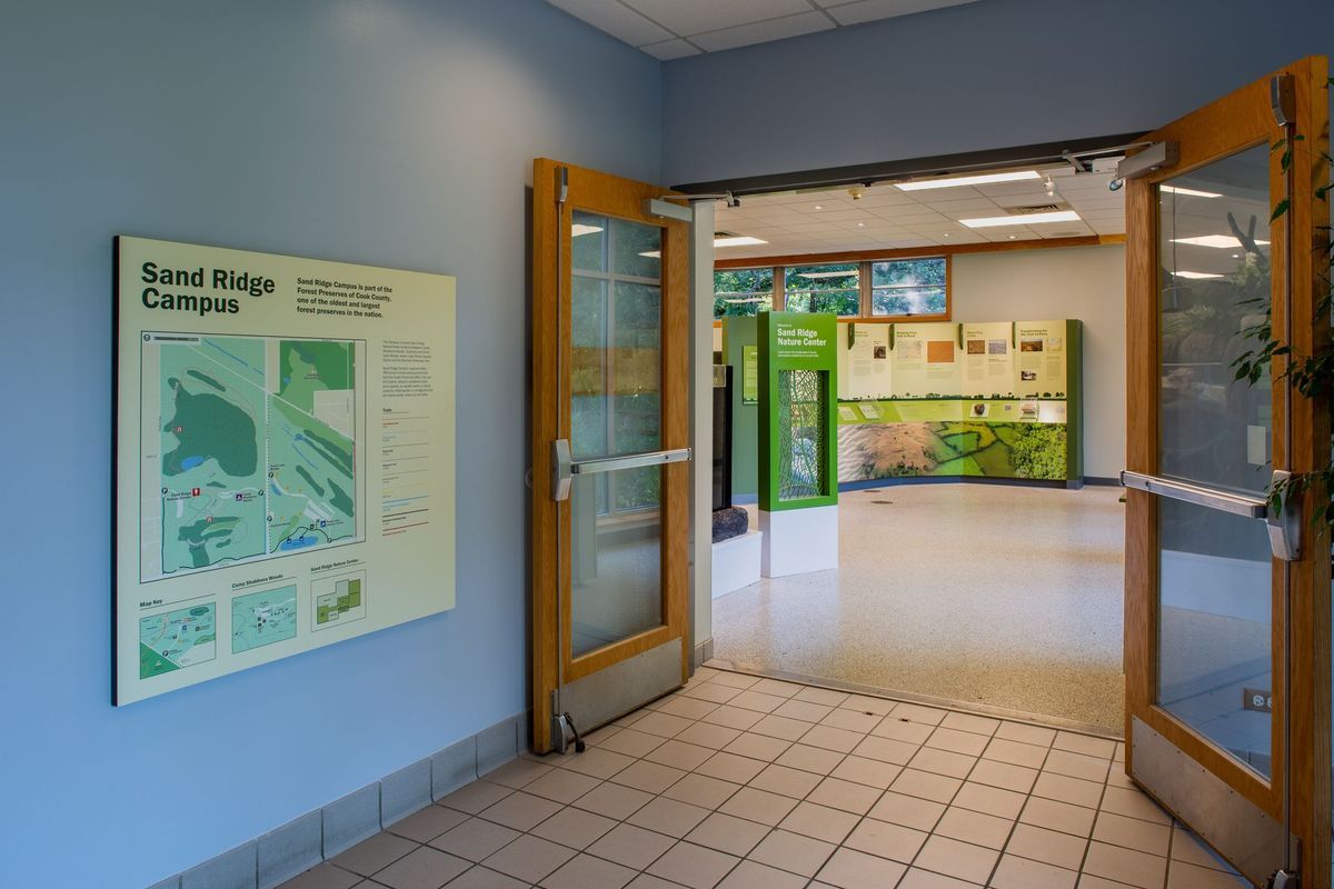 Open doorway into an exhibit space with informational displays. Sign on blue wall, tan tile floor.