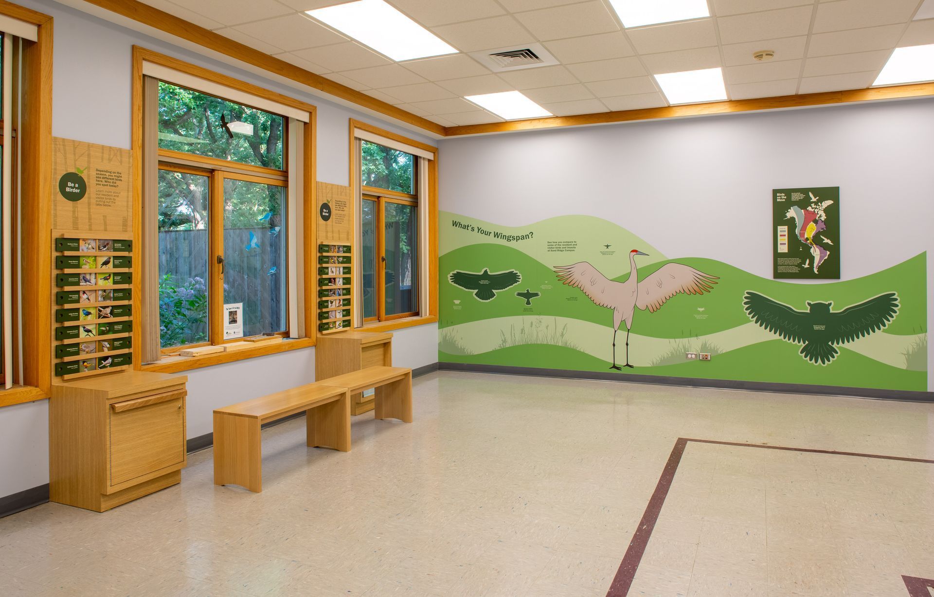 Interior of a nature center with windows, bench, and wall mural of birds in a green landscape.