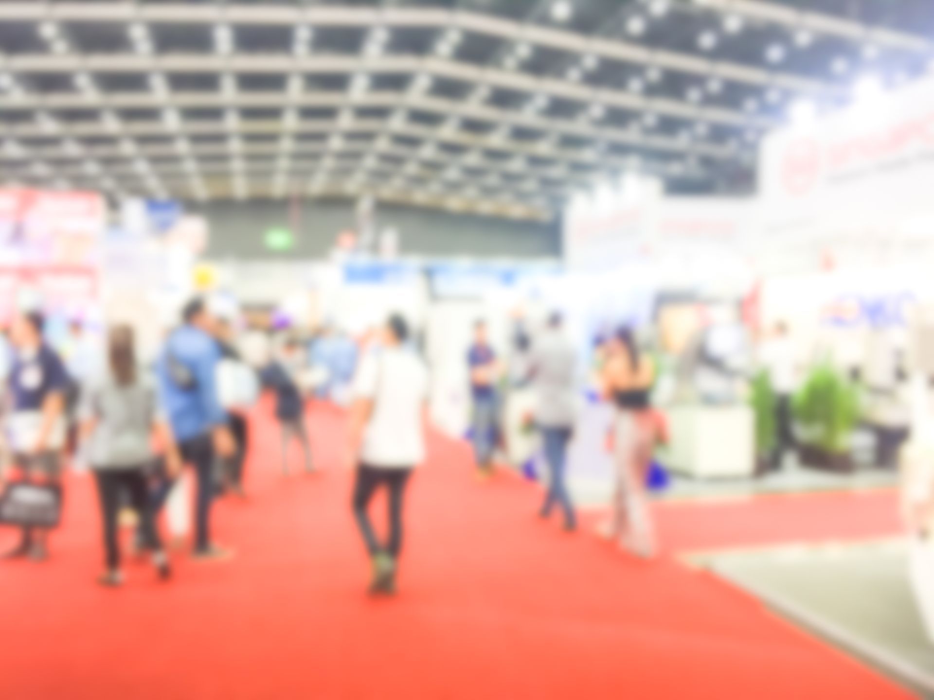 Blurred view of people at a convention or trade show, walking on a red carpet.