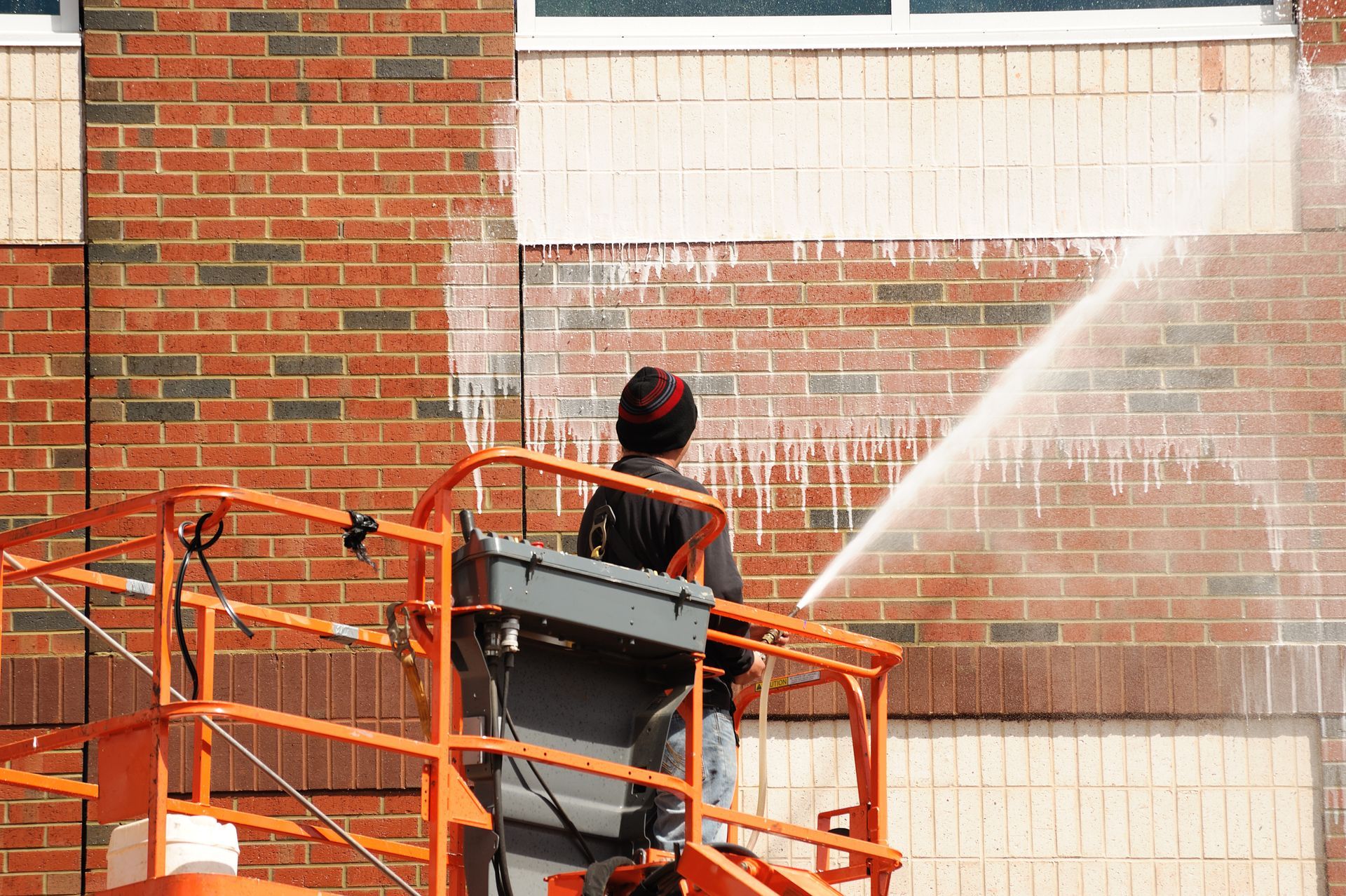 Worker on orange lift spraying water on a brick wall outside a building