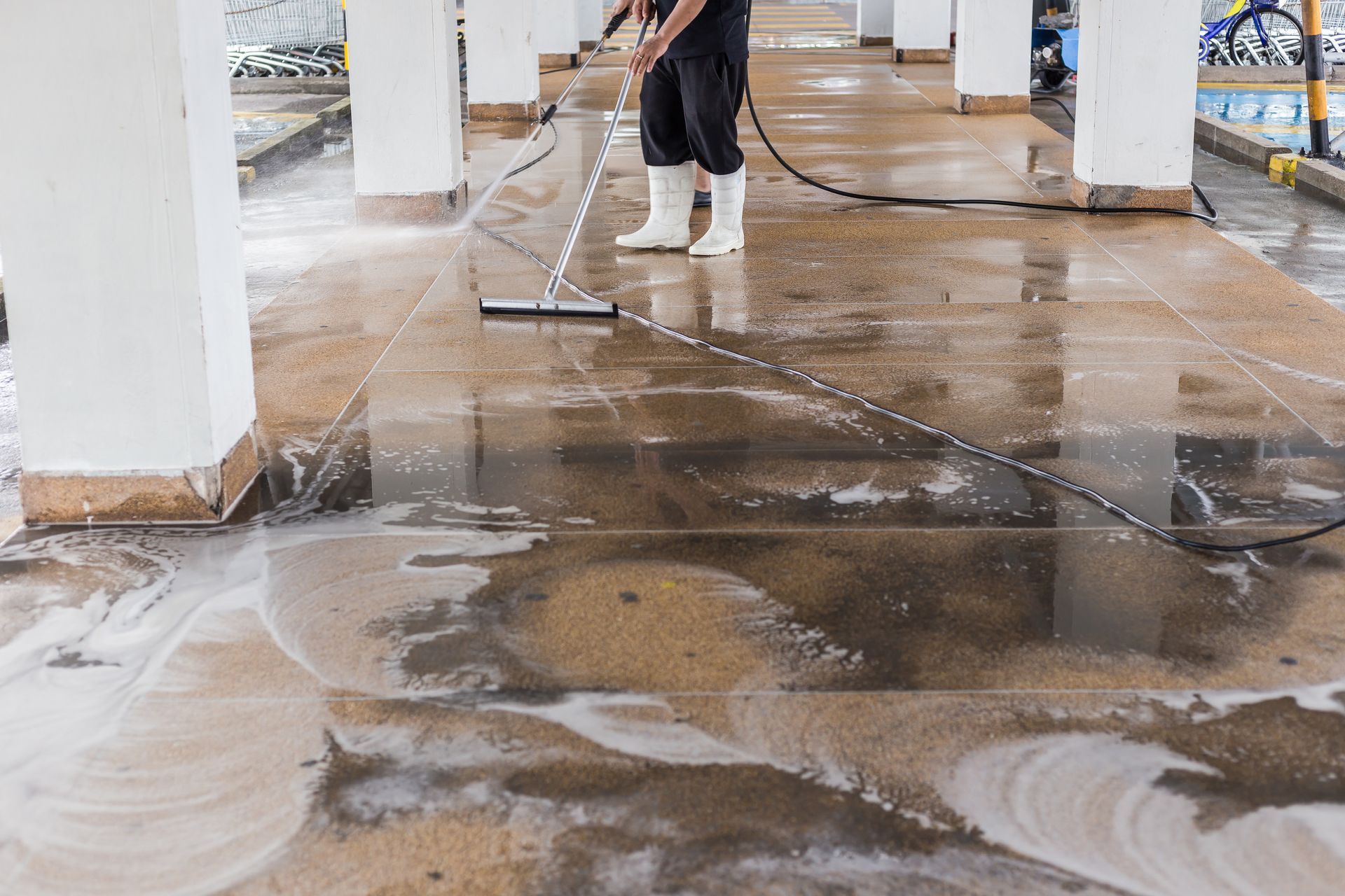 Wet concrete floor being cleaned with a pressure washer in a parking garage.
