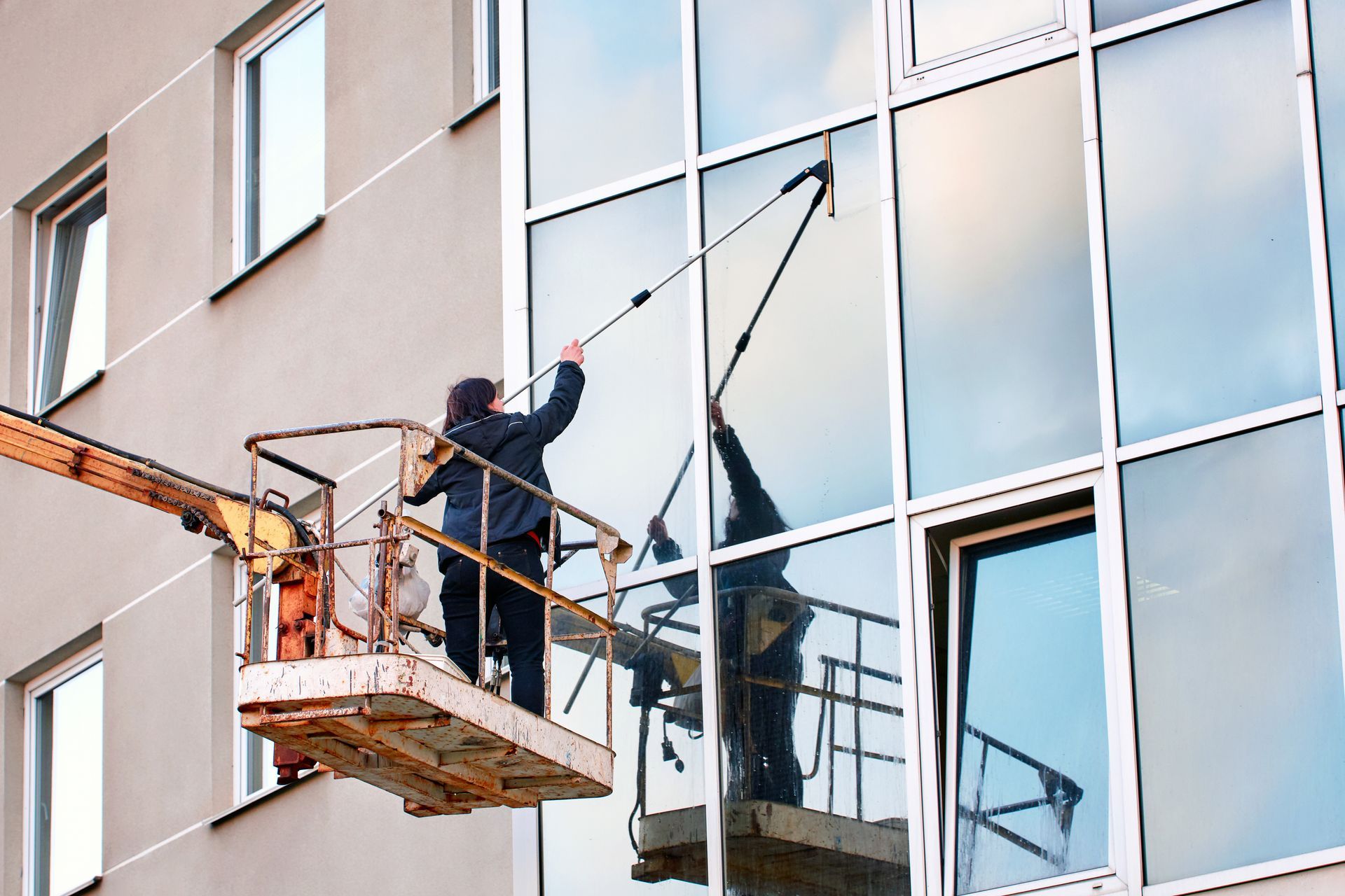 Worker on a lift cleaning a glass building facade