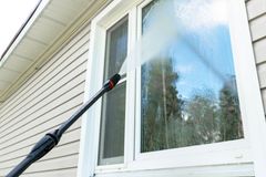 Pressure washing a house window and siding with a long-handled spray wand