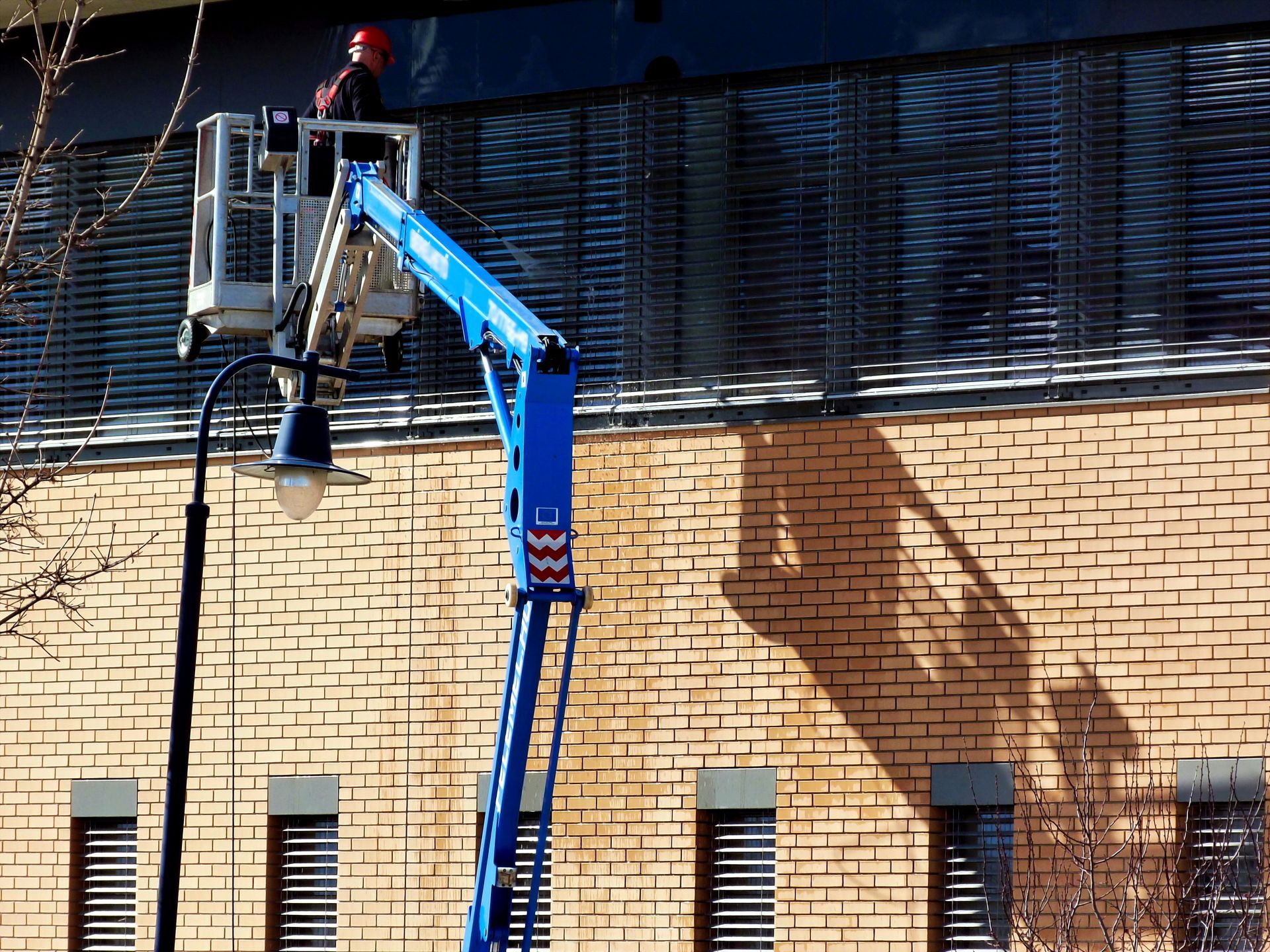 Blue lift platform beside a brick building, with a worker in a red helmet near the top.