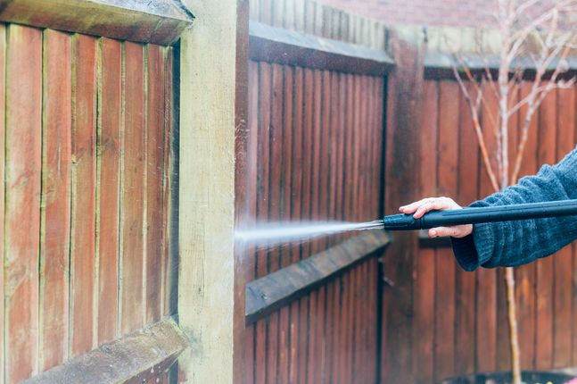 Person pressure washing a wooden fence with a hose outdoors