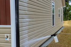House siding being spray painted white along the base of a beige home outdoors