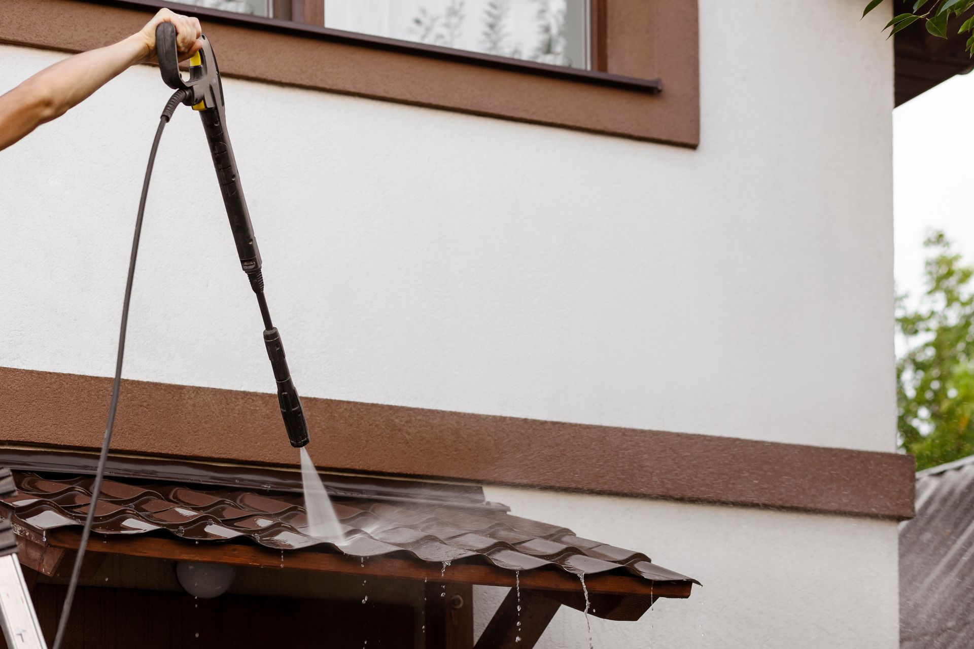Worker pressure-washing a brown awning under a white building wall