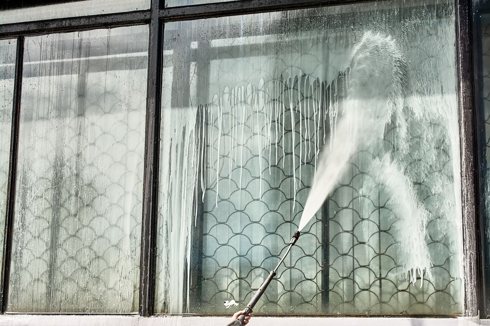 Person pressure-washing a dirty window with a spray nozzle