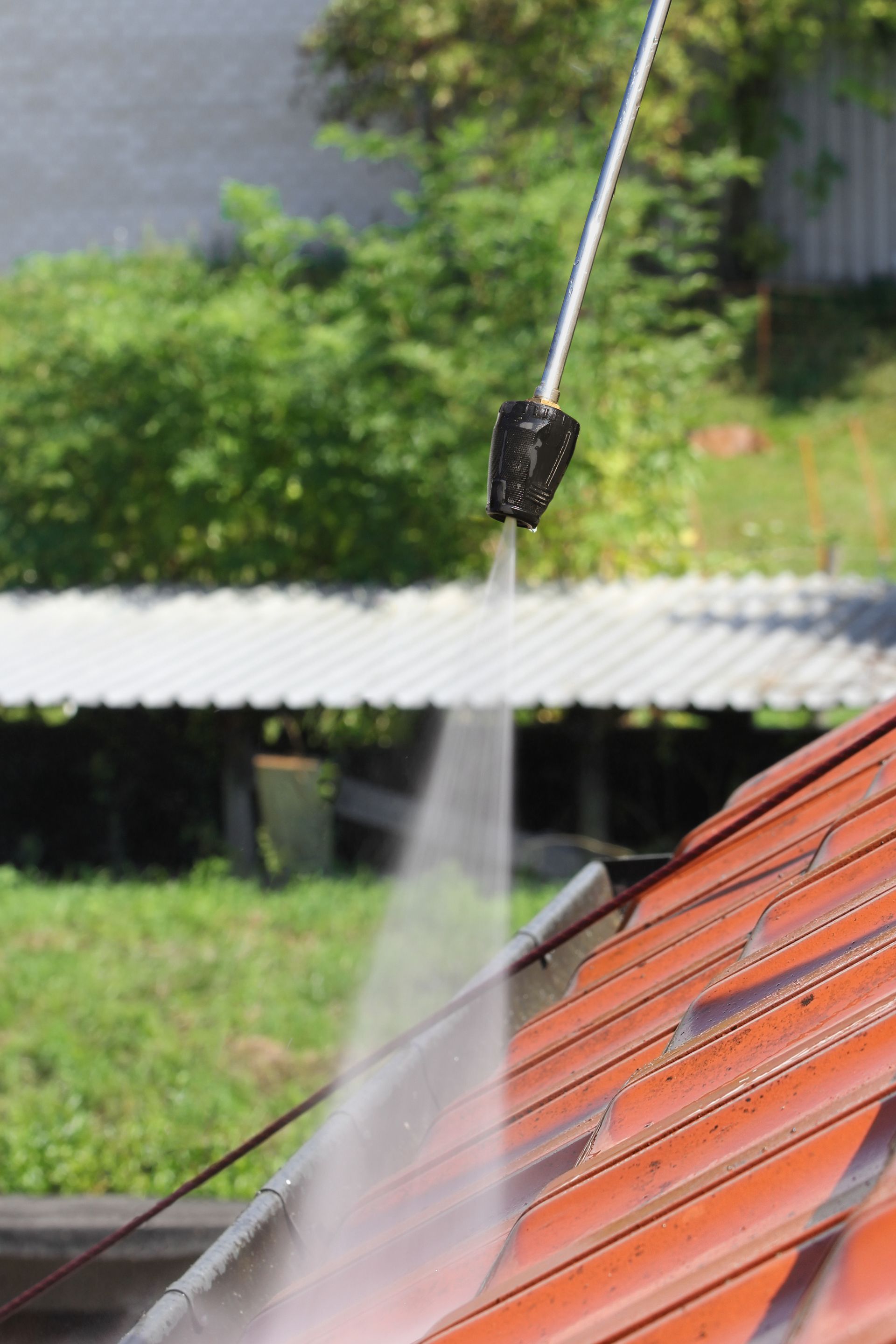 Water spraying onto a red tiled roof from a hose nozzle outdoors