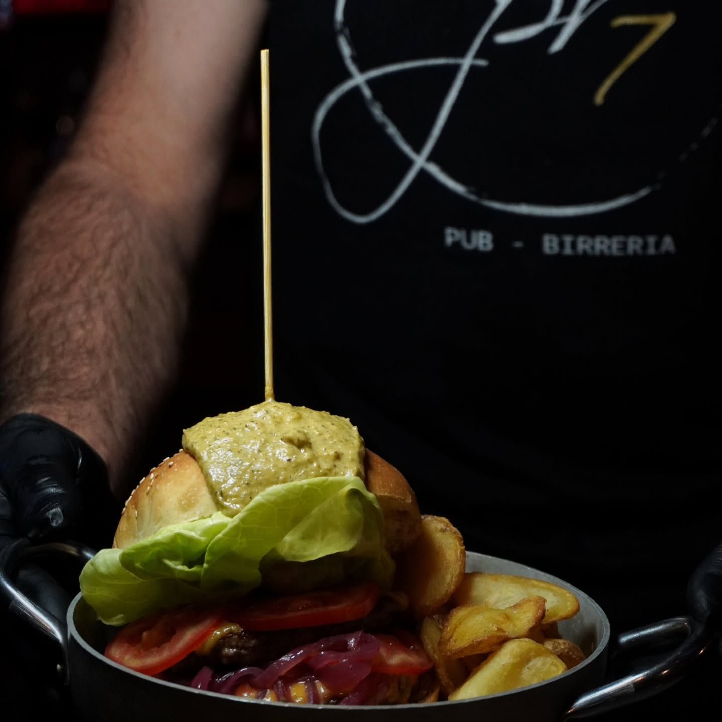 Persona che tiene in mano un hamburger e patatine fritte in una ciotola. L'hamburger è condito con lattuga, pomodoro e salsa