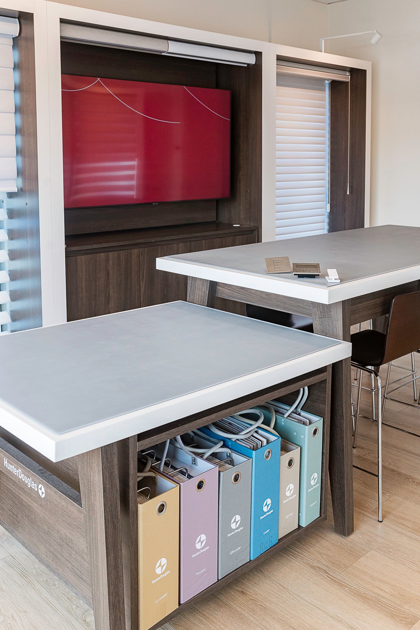 Modern office lounge with white tables, filing bins, and a large wall-mounted TV