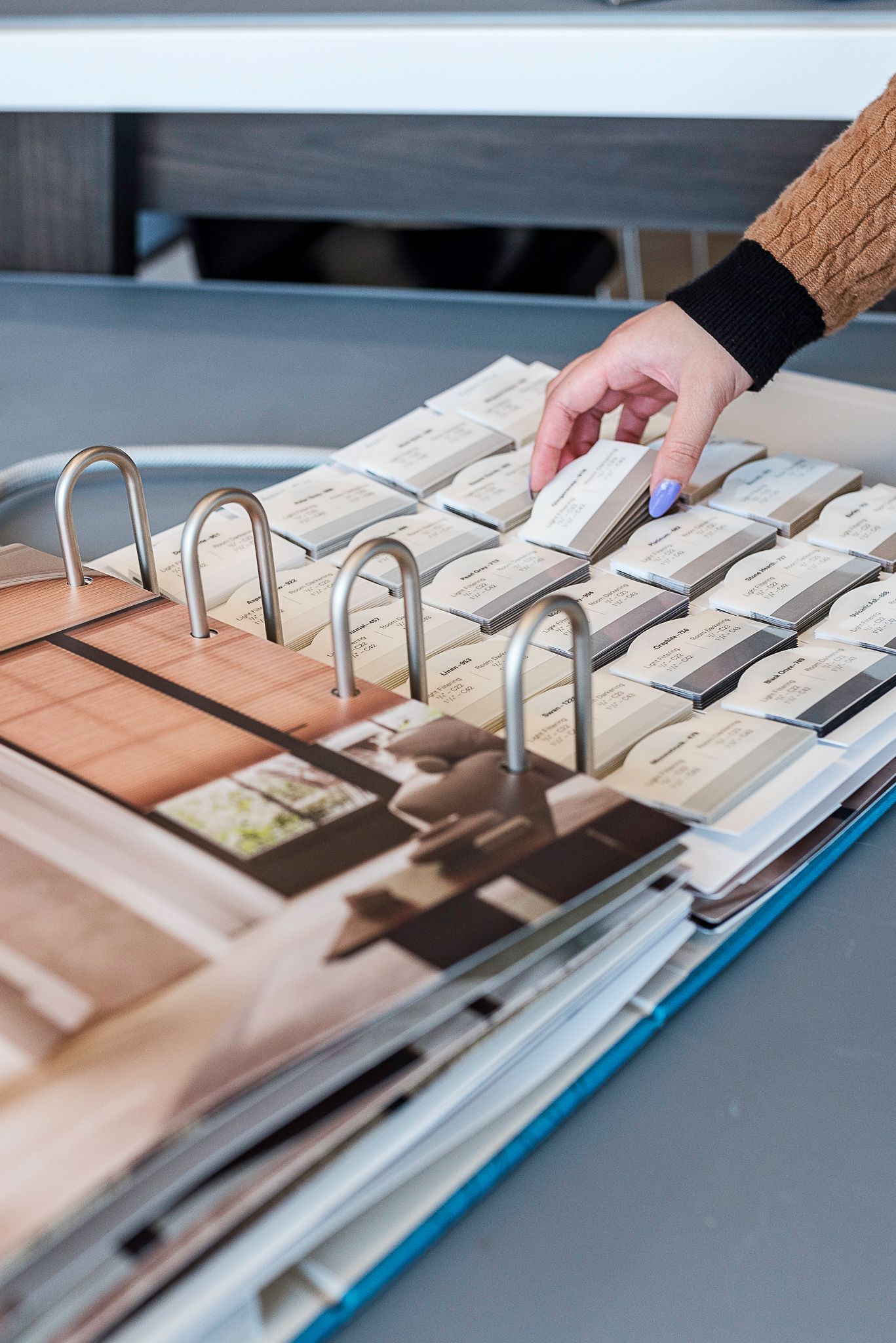 Hand flipping through a large catalog of fabric samples on a table