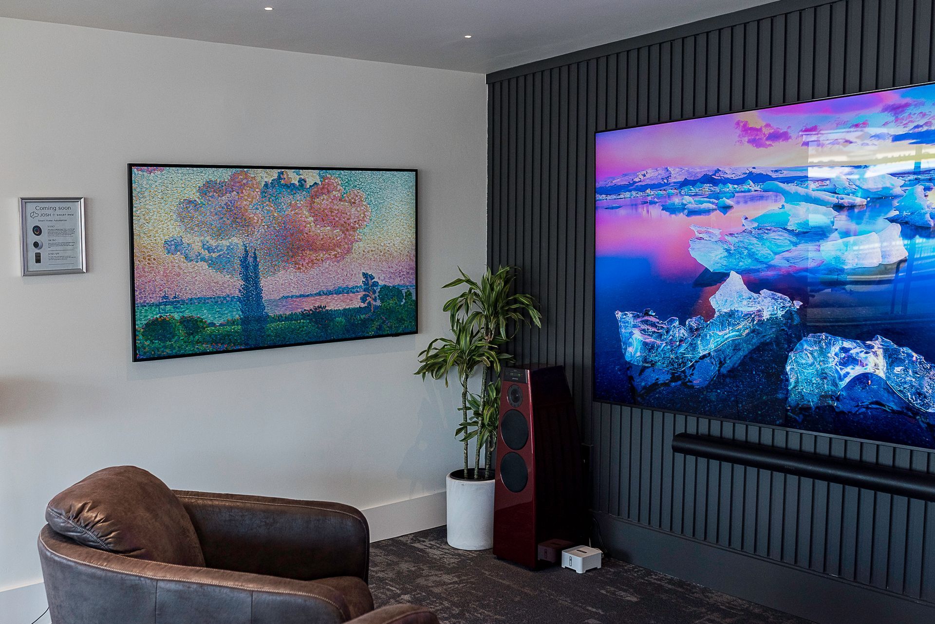 Modern living room with wall-mounted TV, framed art, leather chair, and potted plant.