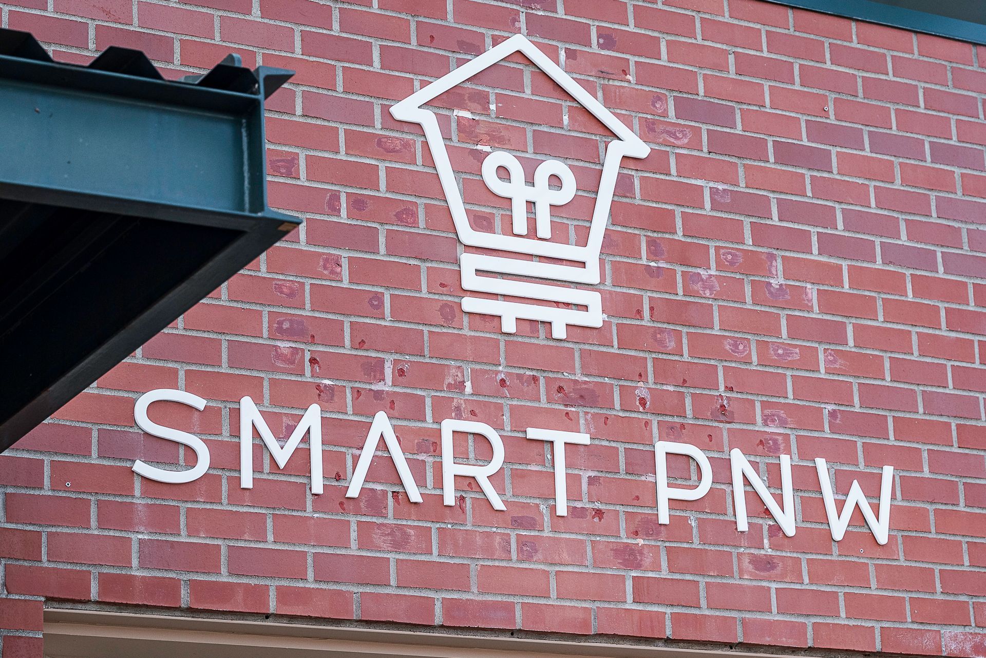 White SMART PNW logo on a red brick wall with a black overhang corner