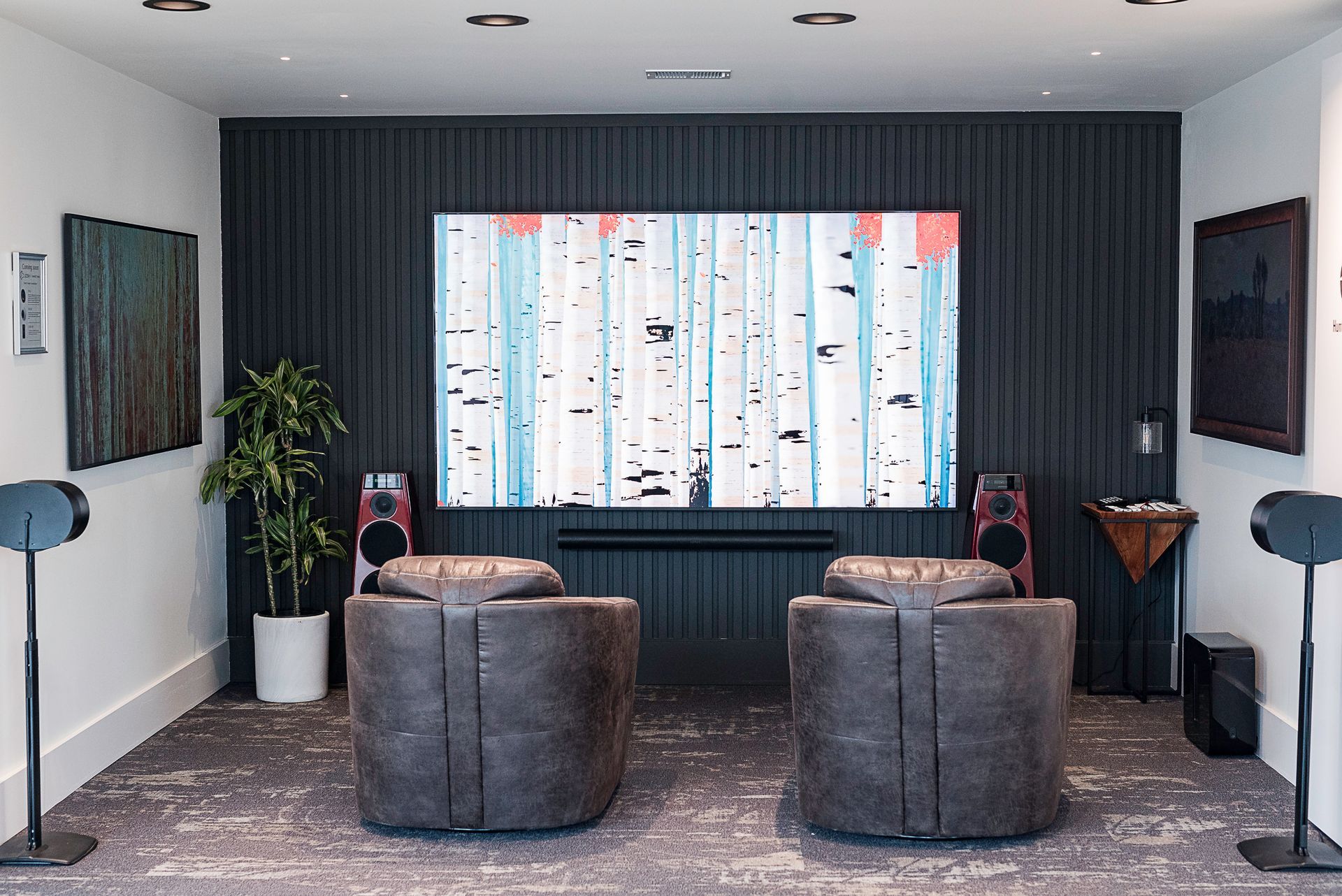 Modern lounge with two gray armchairs facing a large abstract artwork, dark curtains, and potted plants.