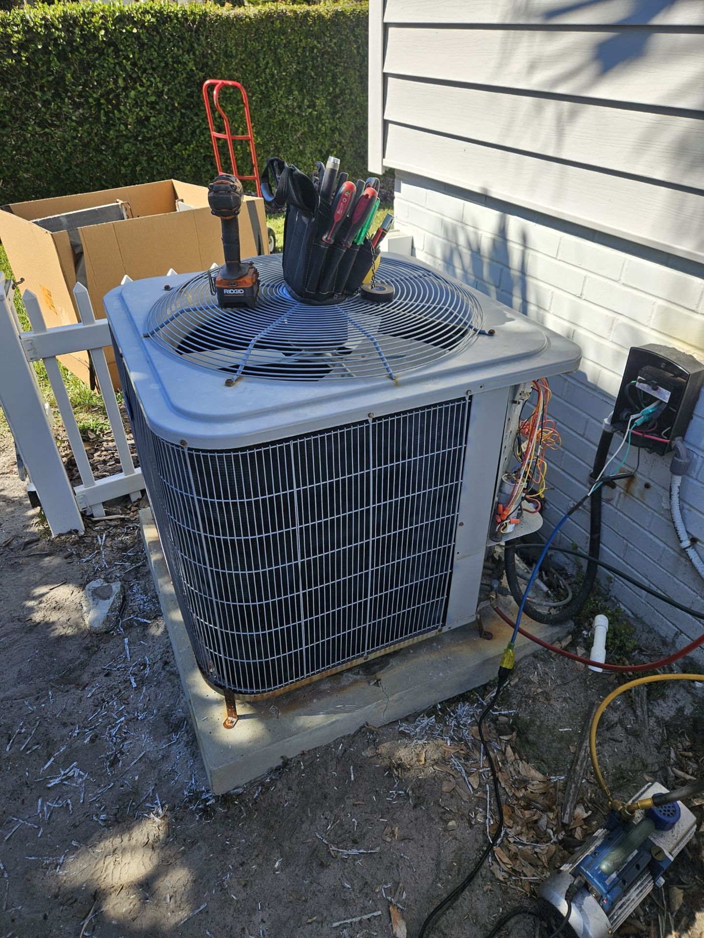 Outdoor air conditioner unit with tools on top beside a house wall