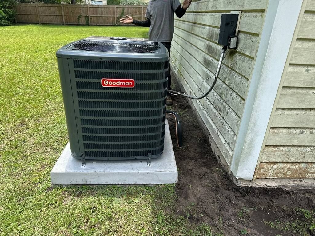 Outdoor air conditioning unit beside a house, set on a concrete pad with an electrical box and hose nearby
