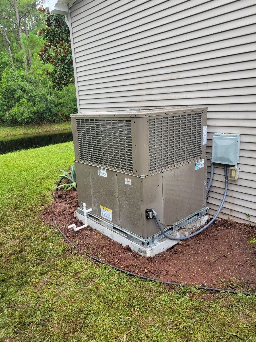 Outdoor HVAC unit beside a house, with ducted enclosure and electrical box on a grassy lawn.