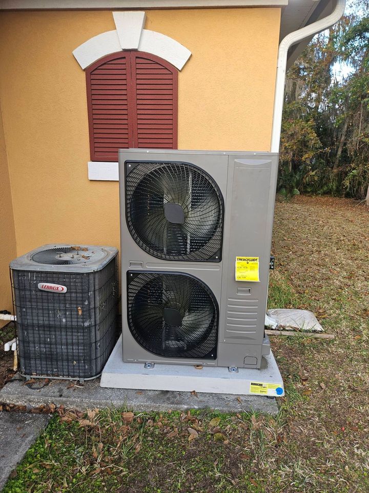 Outdoor air conditioner units beside a yellow house with a red shuttered window.