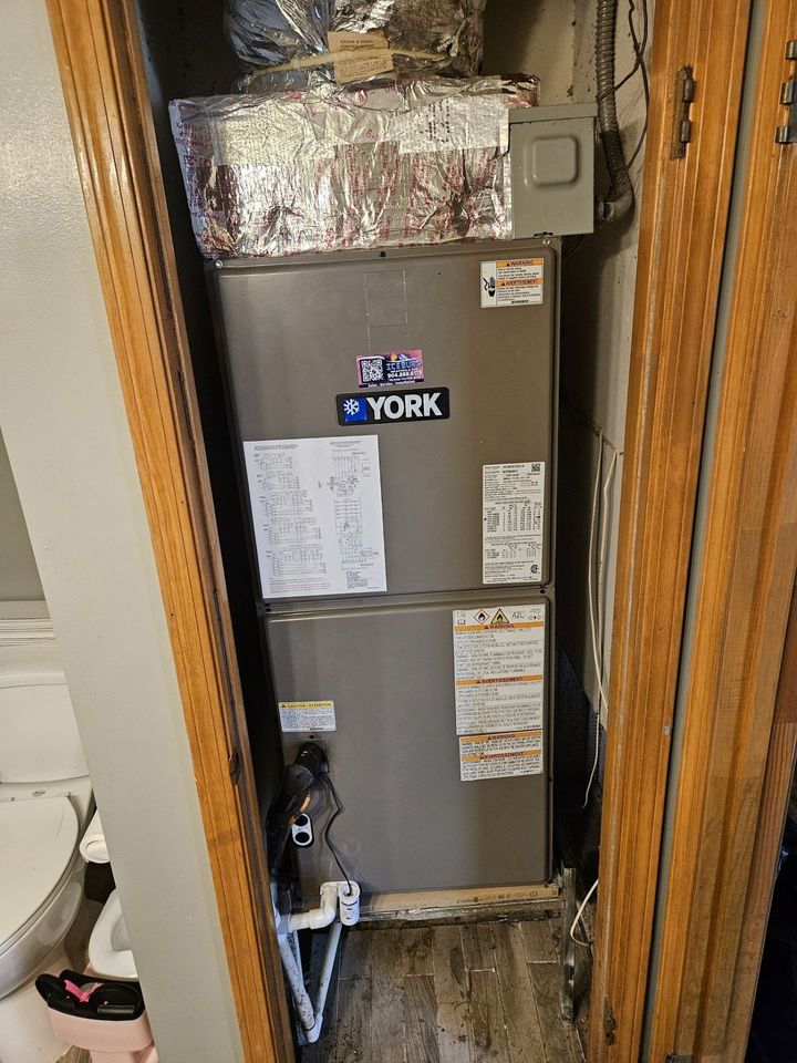 York furnace and HVAC unit in a narrow utility closet with exposed ductwork and wood trim.