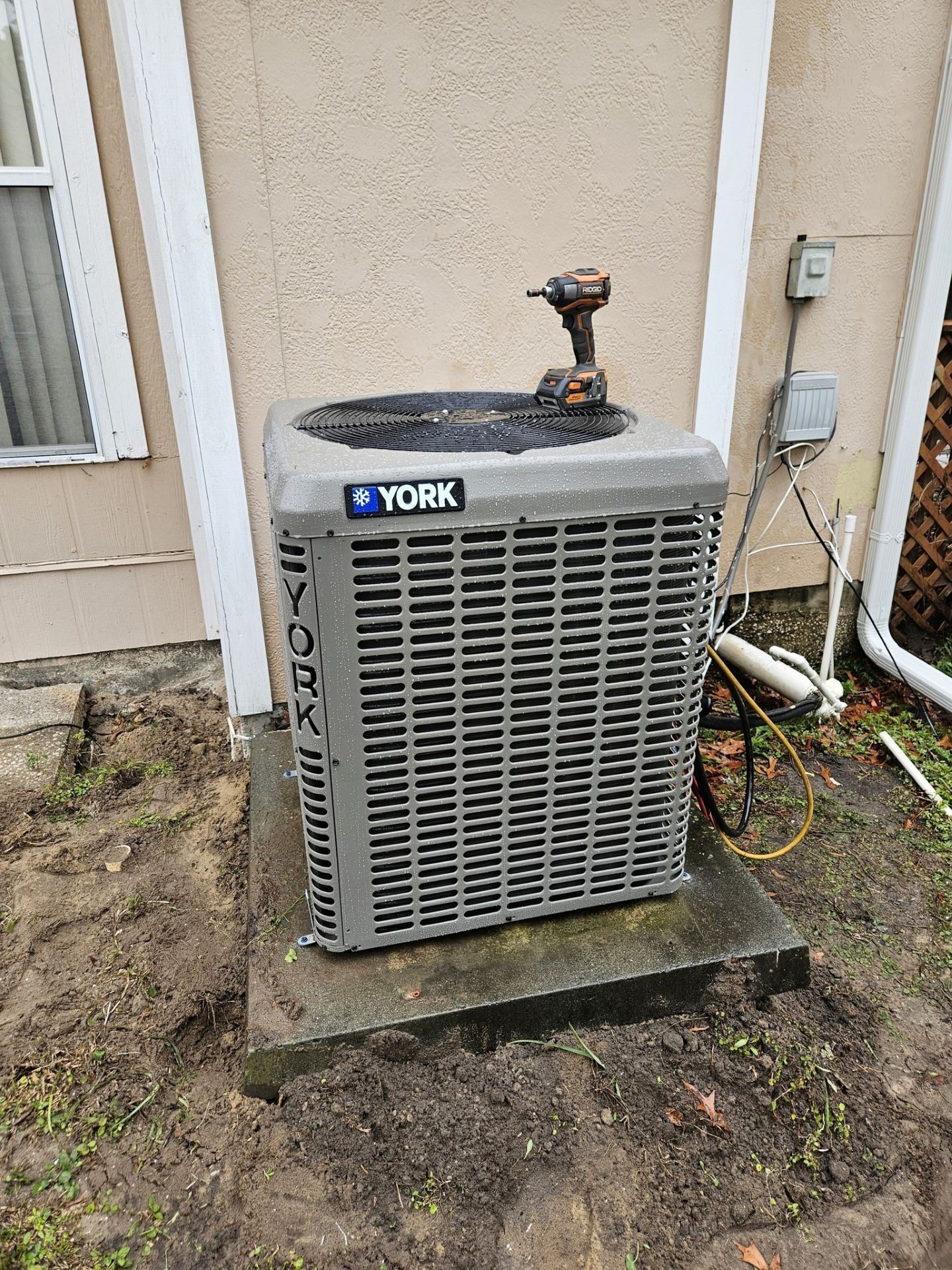 Outdoor York HVAC unit beside a house wall, with a power drill resting on top