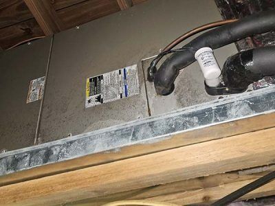 Close-up of a dusty HVAC unit with white insulated pipes and labels in a basement or attic space